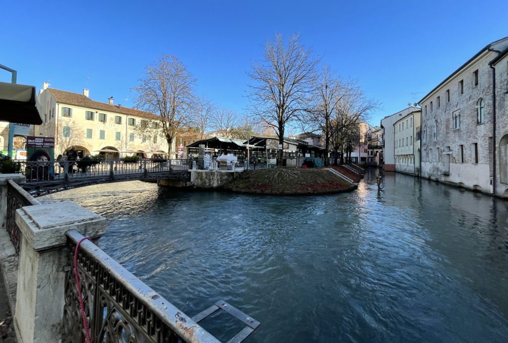 Canal de Treviso junto a la Isola della Pescheria, con puente de hierro, árboles sin hojas y edificios históricos al fondo