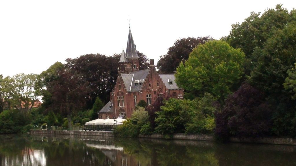 Vista de un restaurante junto al canal con terraza y edificio de ladrillo con torre en Brujas